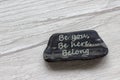 Be here, be you, belong symbol. Beautiful stone with words `Be here, be you, belong` on beautiful white wooden background.