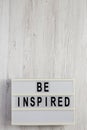 `Be inspired` on a lightbox on a white wooden background, overhead view. Flat lay, top view, from above