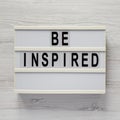 `Be inspired` on a lightbox on a white wooden background, top view. Flat lay, overhead, from above