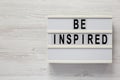 `Be inspired` on a lightbox on a white wooden background, top view. Flat lay, overhead, from above. Copy space