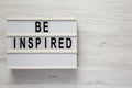 `Be inspired` on a lightbox on a white wooden background, top view. Flat lay, overhead, from above. Space for text