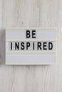 `Be inspired` on a lightbox on a white wooden surface, top view. Flat lay, overhead, from above