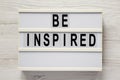 `Be inspired` on a lightbox on a white wooden surface, top view. Flat lay, overhead, from above