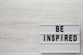 `Be inspired` on a lightbox on a white wooden surface, top view. Flat lay, overhead, from above. Space for text