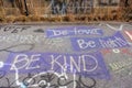Graffiti message of `Be Kind, Be light, Be love` painted in purple banner on asphalt road.