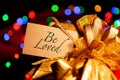 Be loved - text on a gift box label with a large gold bow.