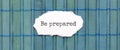 BE PREPARED text on the piece of paper on the green wood background