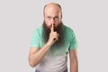 Be quiet. Portrait of serious middle aged bald man with long beard in light green t-shirt standing with finger on lips and showing