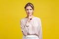 Be quiet! Portrait of serious young blonde woman in casual beige blouse, isolated on yellow background