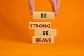 Be strong be brave symbol. Wooden blocks with words `be strong be brave`. Beautiful orange background. Businessman hand. Copy