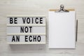 `Be voice not an echo` on a lightbox, clipboard with blank sheet of paper on a white wooden surface, top view. Flat lay, overhea