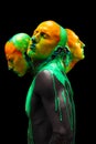 Contemporary artwork. Young bald man, bare-chested model covered with multicolored paints isolated over black background