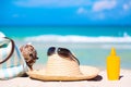 Beach accessories on sand for summer vacation concept. Bag, maracas, straw hat with sunglasses and sunscreen lotion bottle. White