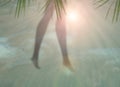 Beach background with blurred silhouettes of female legs, palm leaves and sand.