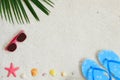 Top view of beach sand with coconut leaves, sunglasses, starfish, shells and slippers.