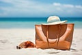 beach bag with sunscreen, sunglasses, and a beach hat on a sandy beach with waves in the background. Generative AI