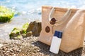 Beach bag with a white eco-friendly tube of sunscreen on a pebble coast near the sea. Travel, holiday at the resort, glasses.