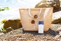 Beach bag with a white eco-friendly tube of sunscreen on a pebble coast near the sea. Travel, holiday at the resort, glasses.