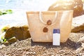 Beach bag with a white eco-friendly tube of sunscreen on a pebble coast near the sea. Travel, holiday at the resort, glasses.