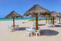 Beach bar - Tiki thatch umbrellas on sandy beach with white plastic chairs underneath and the turquioise sea and very blue sky on