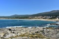 Beach in a bay with forest and small mountain. Rocks, waves and small coastal village. Sunny day, blue sea with foam, clear sky. G Royalty Free Stock Photo