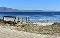 Beach in a bay with wooden boardwalk and vegetation in sand dunes. Blue sea with small waves and clear sky. Sunny day. Spain. Royalty Free Stock Photo