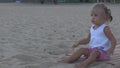 On the beach beautiful baby in a white T-shirt throws a big orange ball in the direction