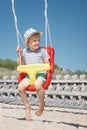 The beach, the blue sky and the happy boy swings in a red-yellow swing. The child smiles and looks to the side, there is free