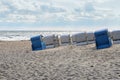 Beach chairs in blue and white from behind standing slanted on the sand in front of the waves on the shore of the Baltic Sea,