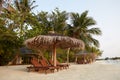 Beach deck chairs under straw umbrellas. Indian ocean coastline on Maldives island. White sandy beach and calm sea Royalty Free Stock Photo