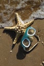 Top view of foaming waves hitting a swimming mask and a starfish lying on a sandy beach. Vacation on the seashore. Sunny weather b Royalty Free Stock Photo