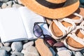 Beach hat on opened book with sunscreen and shoes on pebble beach Royalty Free Stock Photo