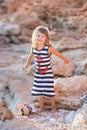 Beach cute girl posing on a rocky beach barefooted with curly hair wearing sailor dress and sun glasses Royalty Free Stock Photo