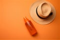 beach essentials flat lay. straw hat and sunscreen oil or lotion on bright orange background