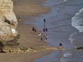 Beach Exploration: Tourists Walking Along Sandy Shoreline with Rocky Cliffs