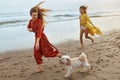 Beach. Girls With Dog Walking Barefoot On Sandy Coast. Fashion Women In Bohemian Clothing With Pet