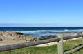 Beach with grass, wooden fence and morning light. Rocks and blue sea with waves and white foam. Sunny day. Galicia, Spain. Royalty Free Stock Photo