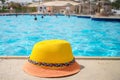 A beach hat is on the background of a pool with people. There is a tourist hat at the pool where the party takes place