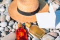 Beach hat on opened book with sunscreen and shoes on pebble beach