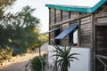 Beach house with bright aqua coloured roof, wooden windows opened, sandy path leading to sea in background. Tropical Royalty Free Stock Photo