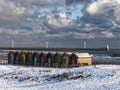 Beach huts in snow with windfarm and lighthouse, Blyth, Northumberland, UK