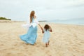 Beach. Kid And Woman In Maxi Dress Walking Along Ocean Coast. View From Back Of Young Mother With Daughter At Resort. Royalty Free Stock Photo