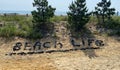 Beach life spelled out with small black rocks on a sand dune