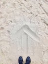 On the beach are a pair of sneakers and a drawn arrow on the sand