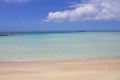 Beach with pink sand and turquoise water and clouds in blue sky.