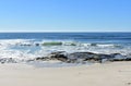 Beach with rocks, bright sand and small waves breaking. Blue sea with foam, sunny day. Galicia, Spain. Royalty Free Stock Photo