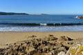 Beach with rocks, wet sand and waves with foam. Blue sky, sunny day, Galicia, Spain. Royalty Free Stock Photo