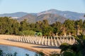 Beach with rows of umbrellas and chairs by the sea in a holiday village during the summer in Italy. Trees and mountains in the