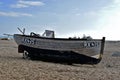 A beach scene, A small wooden fishing boat tilted to the side left on the pebbles of the beach at Dungeness