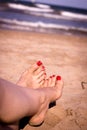 Feet of woman with nails painted red on the sand of the sea Royalty Free Stock Photo